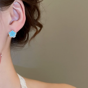 Close-up of blue flower stud earrings with silver edges and micro-set diamonds on model