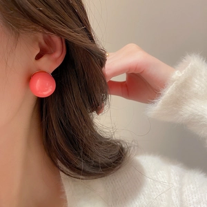 Close-up of pink glossy round stud earring worn by model in soft warm lighting