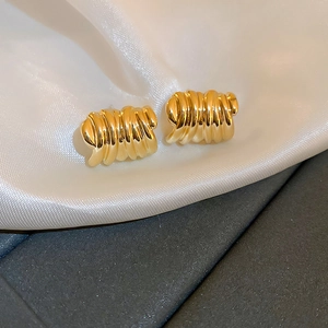 Macro detail of golden geometric spiral earrings with textured finish on white fabric