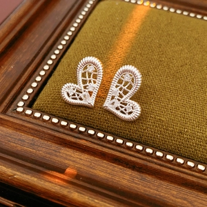 Detail of silver heart earrings with hollow mesh and zircons on green velvet tray