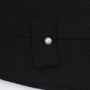 Detailed close-up of black tweed fabric texture with decorative pearl button on pocket