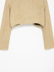 Close-up of golden tweed fabric texture with subtle shimmering sequins on cropped jacket