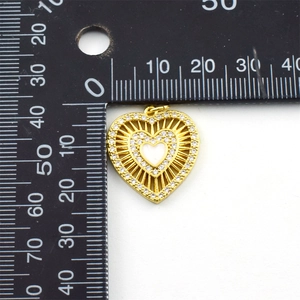 Macro view of gold-plated heart pendant with zircon and enamel next to a scale ruler