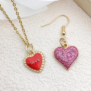 Close-up of golden heart pendants with red enamel and pink glitter with Love engraving