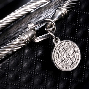 Macro view of silver twisted rope bracelet with a Saint Benedict Medal on black leather