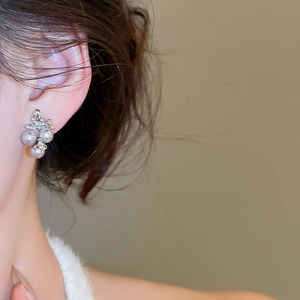 Detail of elegant silver bow pearl earrings with floral accents on a female model