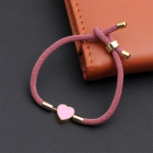 Detailed shot of a pink woven rope bracelet with a gold enamel heart pendant and slide clasp
