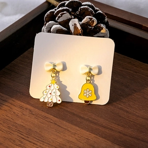 Détail de boucles d'oreilles sapin de Noël asymétriques avec nœuds blancs et cloches