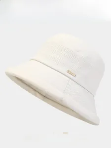 Détail du tissu blanc tissé texturé et de la plaque dorée arth sur le chapeau bob