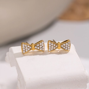 Boucles d'oreilles nœud dorées avec cristaux brillants sur socle en marbre blanc