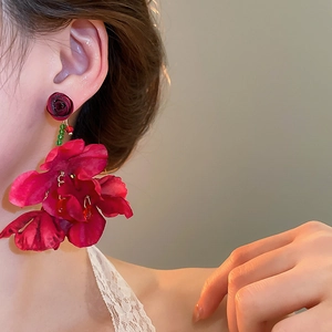Detailed close-up of a model wearing red fabric flower tassel earrings in soft warm light