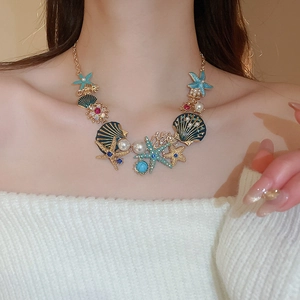 Close-up of a gold necklace with blue starfish and shell charms worn on a model