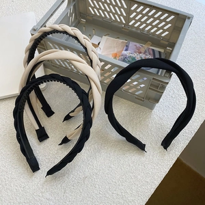 Detail of braided twist headbands in black and beige fabrics on a textured surface