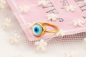 Macro shot of gold Evil Eye ring with blue enamel inlay on a soft decorative background