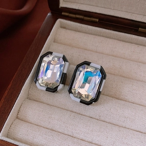 Close-up of rectangle crystal earrings with black and white enamel on a beige velvet box
