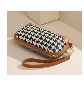 Detail of houndstooth fabric and brown leather wrist strap on stylish clutch bag