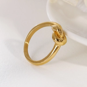 Close-up of a minimalist 18K gold-plated knot ring resting on white ceramic tray