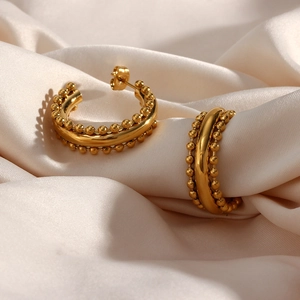 Detail of gold-plated stainless steel hoop earrings with bead trim on silk fabric