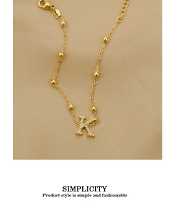 Macro detail of gold letter K pendant with zircon inlay and beaded chain design