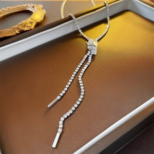 Detail of silver tassel necklace with cubic zirconia and metallic pendant on brown background
