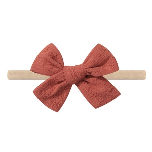 Detailed close-up of a rust-red textured bow on a soft beige elastic baby headband