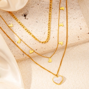 Dettaglio di collane multistrato in oro 18K con ciondoli a cuore su tessuto di seta
