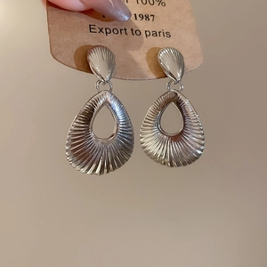 Detailed macro shot of silver teardrop earrings with radial texture on a kraft card