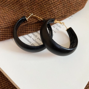 Detail of black leather circular hoop earrings with golden metal accents on tweed fabric