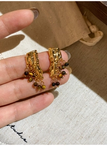 Detail of vintage gold earrings with lava texture and tiger eye beads held by hand