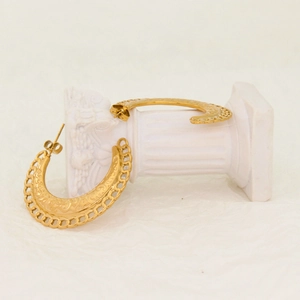 Détail de boucles d'oreilles créoles C dorées ajourées avec motifs en relief sur mini colonne