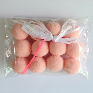 Pink craft pom pom balls and tool in transparent bag with white ribbon bow