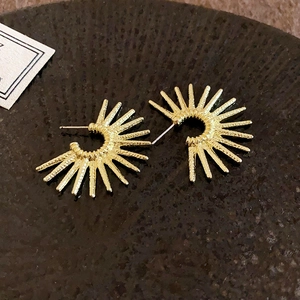 Macro shot of gold sunburst C-shaped earrings with textured finish on a stone tray