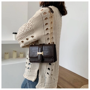 Detail of dark brown crocodile pattern handbag featuring a gold H-shaped metal buckle