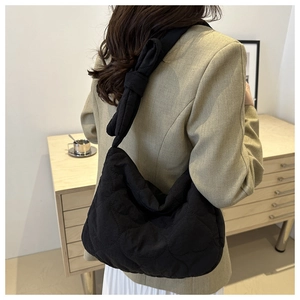 Detailed view of black quilted shoulder bag with knotted strap design on a model