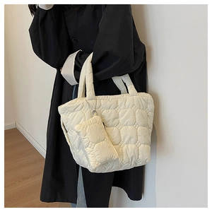 Detail of white quilted tote bag with matching mini pouch on a model in a black coat