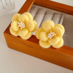 Détail de boucles d'oreilles fleurs en feutre jaune avec perles blanches sur bois