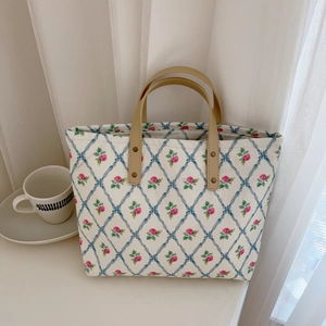 Close-up of floral tote bag with brown faux leather handles and metal rivet reinforcement