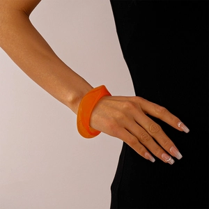 Close-up of a wide translucent orange acrylic resin bangle on a woman's wrist