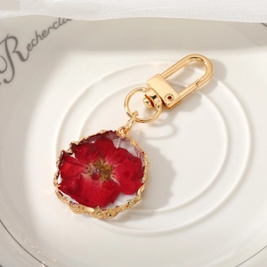 Detail of red dried flower keychain in resin pendant with irregular gold metal edging
