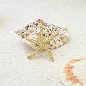 Close-up of a gold starfish pendant with sparkling crystals on a natural seashell
