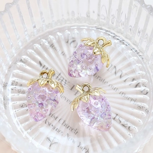 Macro shot of three purple acrylic strawberry pendants with gold metal leaves and glitter