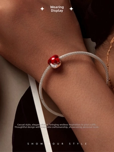 Close-up of a silver woven bracelet featuring a vibrant red enamel apple charm on a wrist