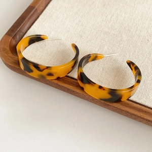 Detail of leopard print C-shaped resin earrings on linen and wooden tray background