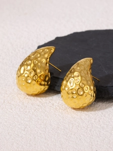 Macro detail of teardrop gold stud earrings with hammered metal texture on black slate