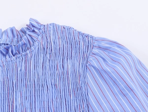 Détail de la texture smockée et du col à volants sur chemise rayée bleue pour femme