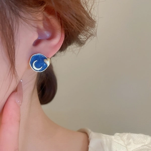 Close-up of blue enamel heart moon earring worn by a model showing artistic detail
