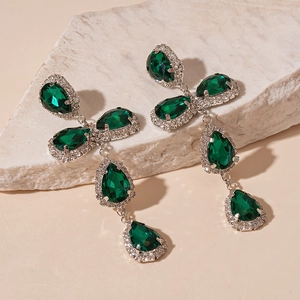 Detail of green teardrop earrings with crystals and silver base on a stone texture