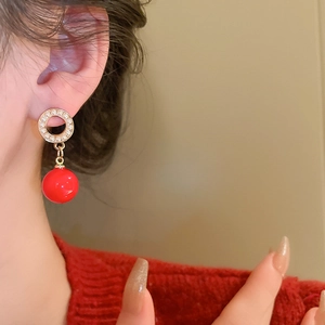Close-up of a model wearing golden geometric hoop earrings with pearls and red beads