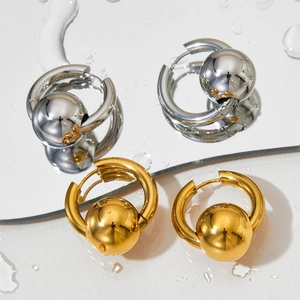 Minimalist ball charm hoop earrings in polished gold and silver finishes on water mirror