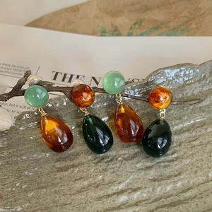 Close-up of resin waterdrop earrings in amber and emerald green on rustic branches